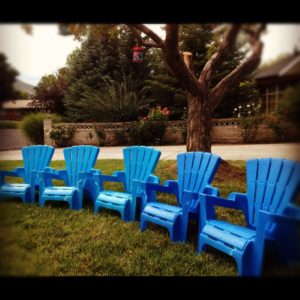 Row of blue plastic chairs lined up outdoors on grass.