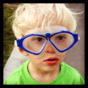 A young boy wearing oversized blue goggles and a green shirt.