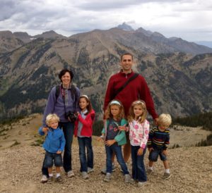 Family of six posing on a mountain trail with cloudy skies.