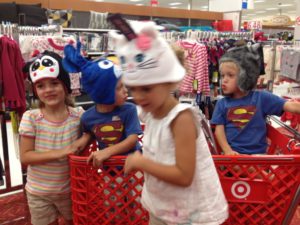 Children in superhero and animal hats playing in a store cart.