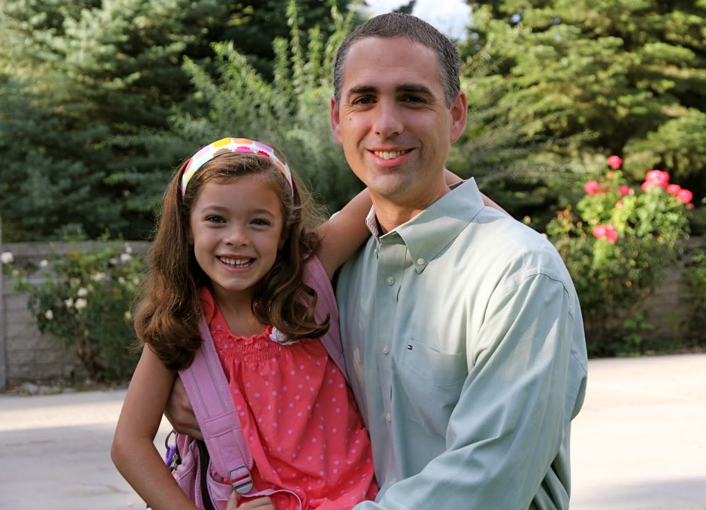 A man and young girl smiling outdoors with greenery behind them.
