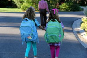 Two young girls with backpacks walking hand in hand outdoors.