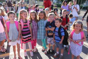 A group of smiling children with backpacks standing outdoors.